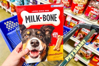 person holding a box of milk bone dog treats over a petsmart cart