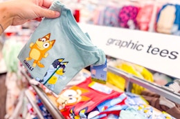 person holding up a bluey toddler tshirt in front of a display of graphic tees