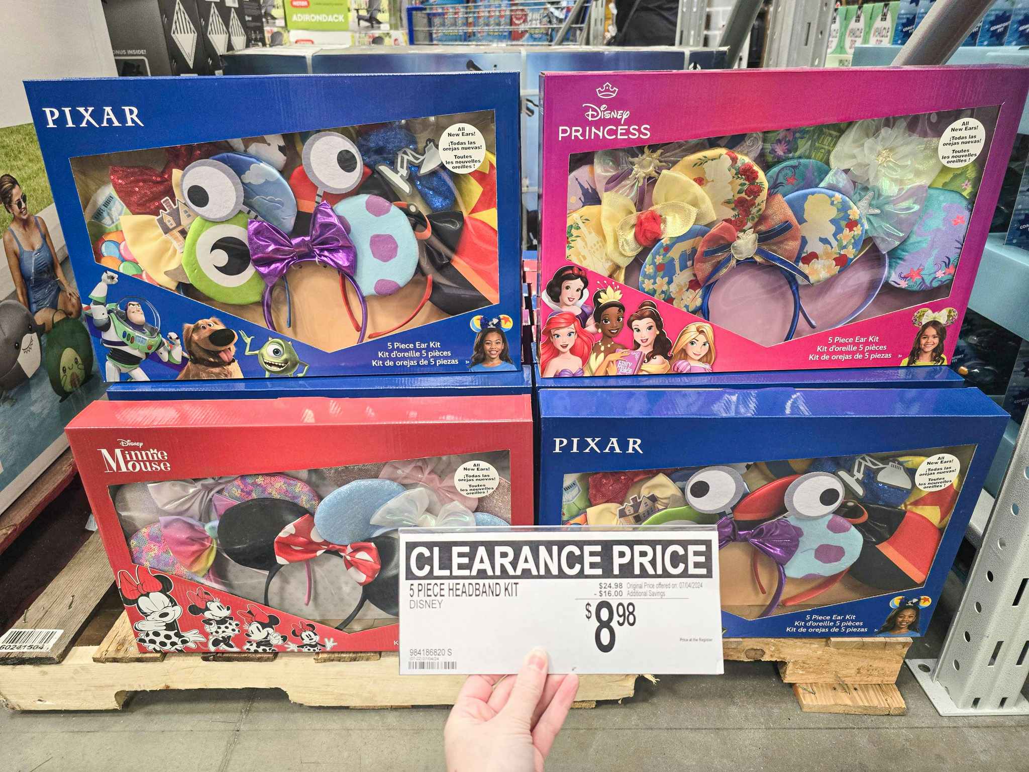 person holding a clearance sign for $8.98 in front of sets of disney ears