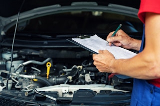 Mechanic with a clipboard in front of an open car engine