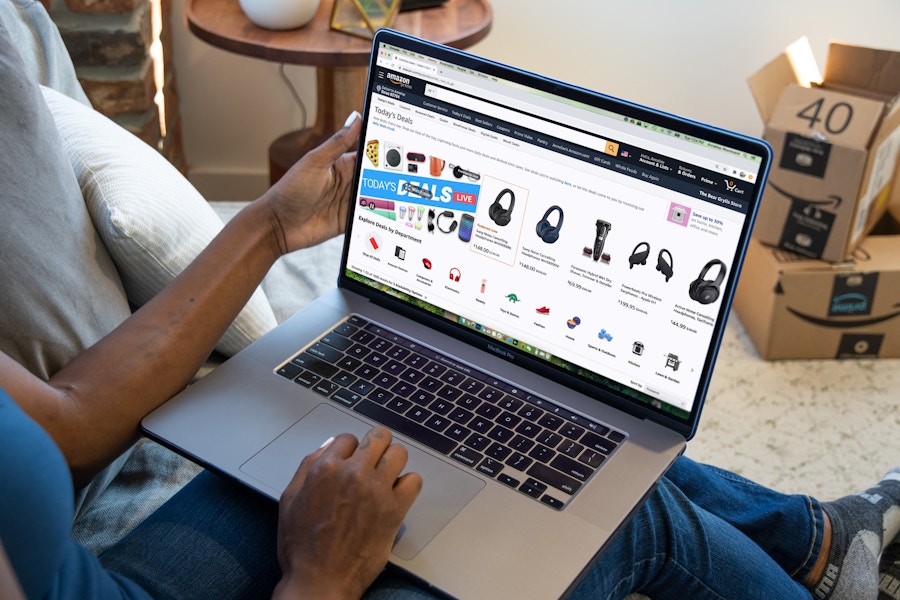 A person sitting on a couch, using a laptop that is displaying Amazon's daily deals on their website.