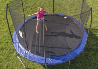 A child jumping on a large Skywalker trampoline in a backyard.