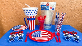A bunch of Fourth of July essentials and party supplies on a table with a blue tablecloth