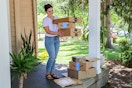 a woman standing on her porch picking up amazon boxes