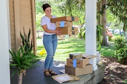 a woman standing on her porch picking up amazon boxes
