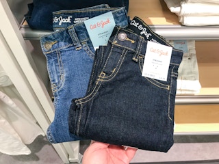A person holding some pairs of Cat & Jack straight fit kids jeans in front of a shelf at Target.