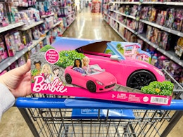 hand holding a barbie convertible car toy on walmart cart