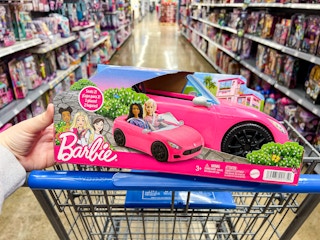 hand holding barbie convertible car toy over walmart cart