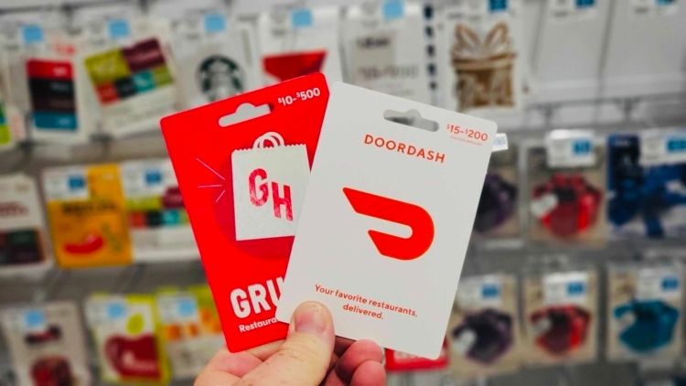 Hand holding Doordash and Grubhub gift cards in front of a gift card display