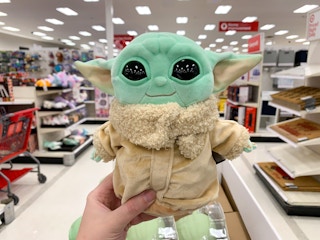 A person holding up a plush baby yoda toy at Target