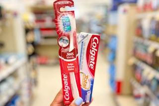 hand holding a Colgate Manual toothbrush and a box of Colgate Total toothpaste in aisle
