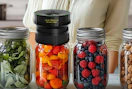 a mason jar sealer on jar full of fruit next to more jars