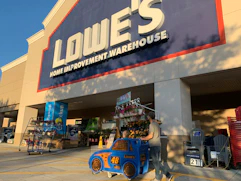 A dad and child in lowes car shopping cart walking into lowes store
