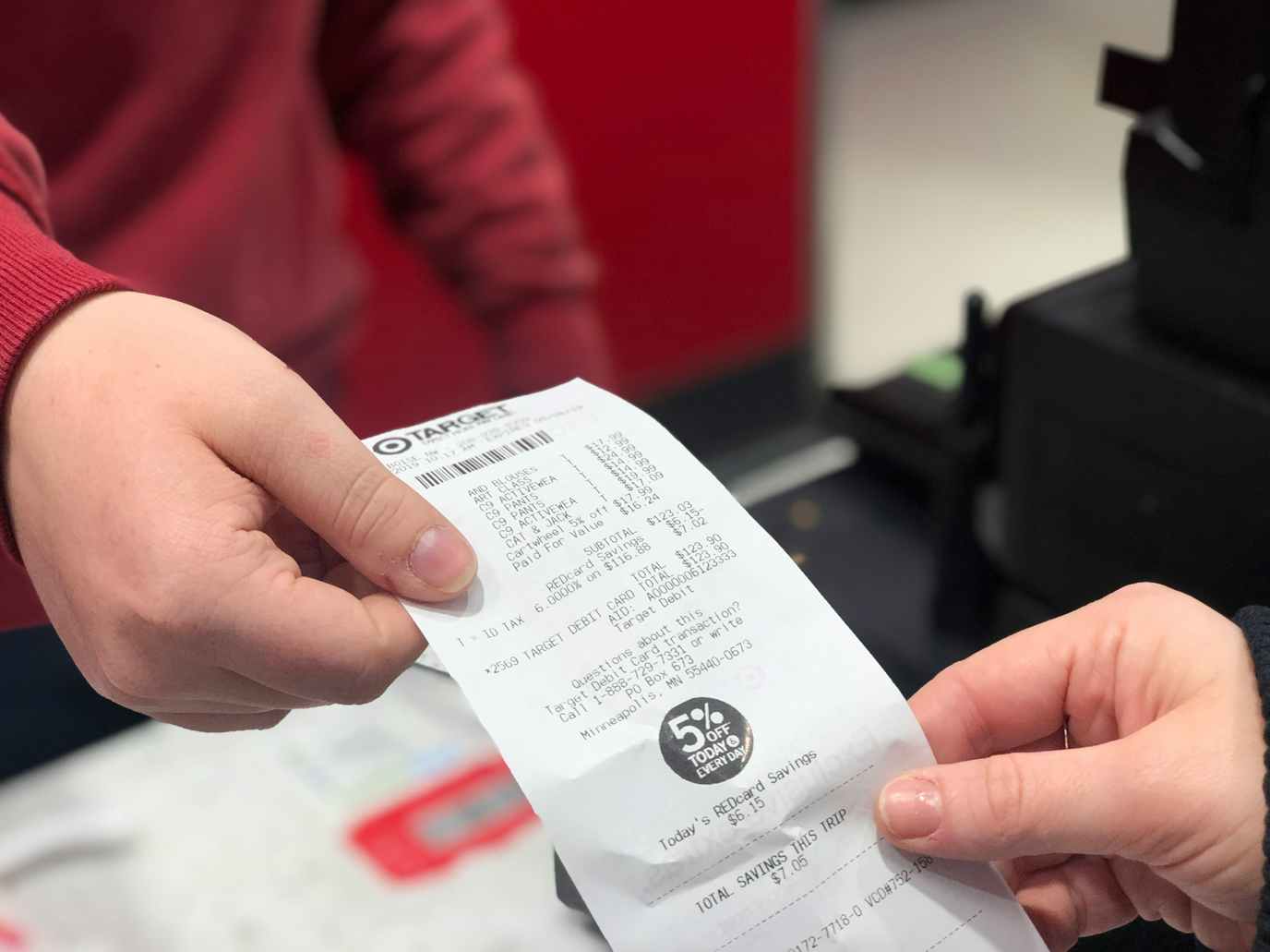 A customer's hand giving a Target receipt to a Target employee at the return counter.