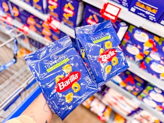 hand holding two bags of barilla tortellini pasta in walmart aisle