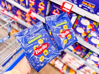 hand holding two bags of barilla tortellini pasta in walmart aisle