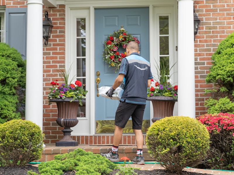 An Amazon delivery van driver dropping a package on a front porch.