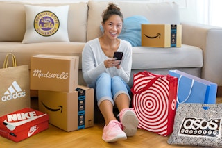 a college student sitting in front of a couch with a bunch of shopping bags and shipping boxes