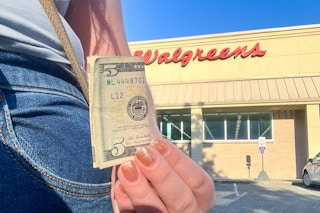 person holding $5 bill in front of walgreens store