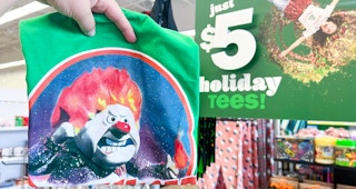 Someone holding up a $5 tshirt in front of a sign inside Five Below