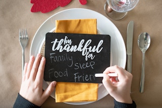 A person using chalk to write on a small chalk board that says "I'm thankful for".