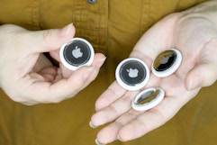 two hands holding four apple airtags