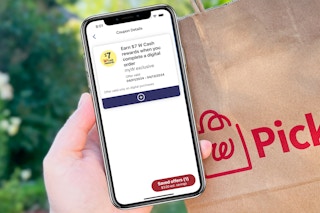 hand holding a smartphone with a walgreens cash booster coupon next to a walgreens pickup bag