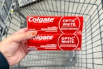 hand holding two tubes of colgate toothpaste over a shopping cart