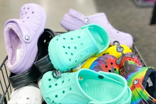 A shopping cart filled with pairs of Crocs inside a store.