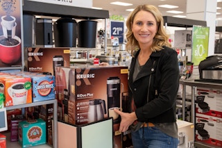 Woman smiling for the camera while holding a Keurig box inside Kohls.