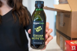 A woman holding a bottle of Amazon Fresh Olive Oil.