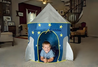 young child laying on stomach inside rocket ship tent set up in living room