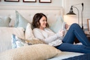A woman lying on her bed, smiling at something on her iPad.
