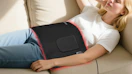 a person laying on a couch with a red light therapy pad on their stomach