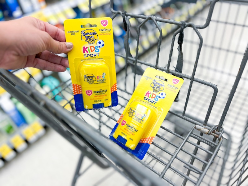 Hand holding sunscreen in front of shopping cart