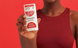 person holding a stick of schmidts coconut & kaolin clay deodorant on a red background