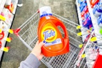 person holding a large bottle of tide detergent over a cart