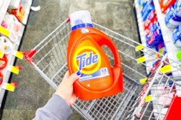 person holding a large bottle of tide detergent over a cart