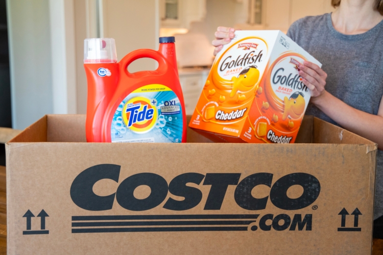 A person pulling gold fish crackers and tide from a Costco.com shipping box.
