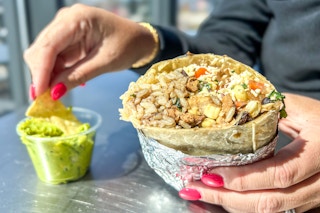 a person holding up a burrito and dipping a chip into guacamole