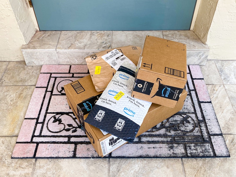 A pile of Amazon boxes and Amazon packing envelopes sitting on a doormat outside a front door.