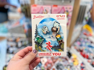 A hand holding Bob Ross themed shoe charms at the Croc store