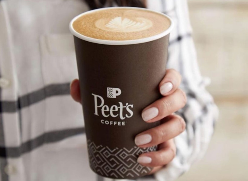 A person holding a cup that says Peets filled with foamy coffee