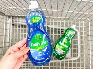hand holding bottle of Palmolive dish soap in front of shopping cart with another bottle inside