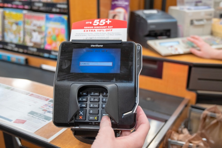 Person entering Fred Meyers reward number on a card reader at a Fred Meyer checkout lane