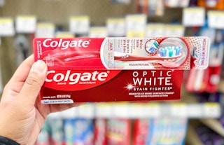 hand holding box of Colgate Optic White toothpaste and a Colgate manual toothbrush in aisle
