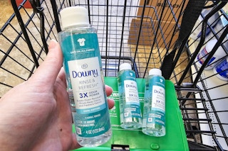 person holding a bottle of downy rinse and refresh over a cart with more bottles in it