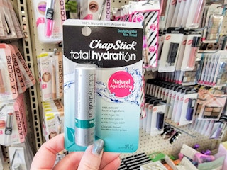a hand holding up chapstick in a store aisle