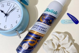 a can of dry shampoo next to a clock and scrunchie