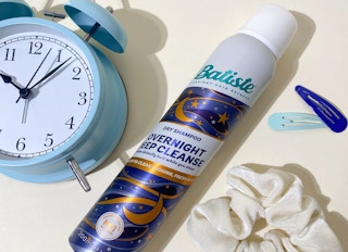 a can of dry shampoo next to a clock and scrunchie